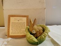Photo of the front view of the ceramic rabbit figurine nestled in lettuce leaves, with informational card in the background.