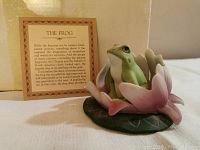 Photo showing the frog figurine sitting on its hind legs in front of its folklore card with text titled 'The Frog'.