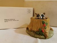 Raccoon peeking from behind tree stump figurine with original Franklin Porcelain box in background.