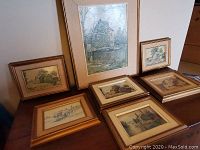 Seven framed paintings by James Lorimer Kierstead arranged on a table showing variety of mill and rural scenes.