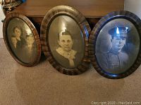 Three antique rounded oval wooden frames with black and white portraits, showing front view on carpet.