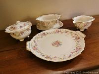 Photo showing all four pieces: gravy dish with underplate, covered sugar, creamer, and serving plate with floral and gold trim.