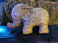 Side view of the floral fabric stuffed elephant toy with visible tear on the head and natural lighting on a dark background.
