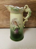 Front view of the vintage porcelain pitcher showing painted lady and floral motif, scalloped rim with gold accents, and gradient color from cream to green.