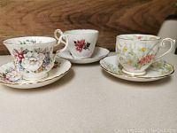 Three teacups with matching saucers arranged side by side showing overall floral designs and condition