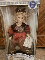 Front view of porcelain doll in original box showing doll in detailed Victorian-style dress and collector edition label.