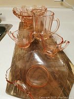 Full set of pink glassware including serving plate, bowl, pitcher, creamer, and sugar bowl with lid arranged on wooden surface.
