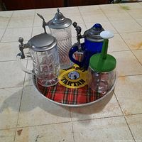 Three glass beer steins, nut chopper, and serving tray viewed together on countertop showing lot contents.