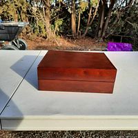 Closed rectangular wooden memory box with smooth reddish-brown finish.