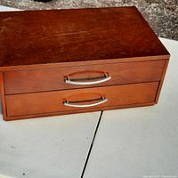 View of the front of the wooden jewelry box showing two drawers with silver curved handles and surface scratches.
