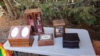 Overview photo showing six assorted jewelry boxes arranged on a white table outdoors, with visible wear and varied styles and sizes