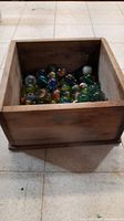 Wooden rectangular box filled with assorted colorful glass marbles, showing wear.