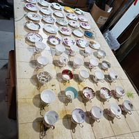 Overview of 39 assorted vintage teacups and saucers arranged on table, showing various floral and gold-trimmed designs