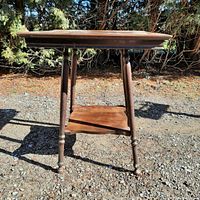 Front view of the wooden parlour table showing the square top, turned legs, lower shelf, and visible damage to leg.