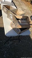 Photo of three weathered wooden crates on a white folding table outdoors, showing rustic condition and branding.