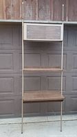 Frontal image showing tall tension pole desk with three wooden shelves and upper storage cabinet in front of a garage door.
