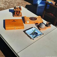 Tobacco related items displayed on a table including two wooden cigar boxes, a wooden pipe stand with pipes, ceramic ashtray with horse design, and a wooden pipe accessory set.