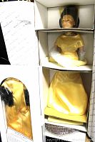 Porcelain doll in original white compartmentalized box wearing yellow satin gown, head wrapped in plastic and netting.