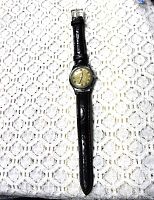 Full view of the vintage Fedcal De Luxe Enicar wristwatch laid flat on lace fabric, showing entire watch and black leather strap.