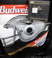 Photo showing the black 1993 Stadium Club Football Members Only binder placed on a folded plastic promotional banner featuring a large Raiders football helmet and Budweiser Bud Light branding with gold fringe visible.