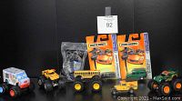 Photo showing 7 diecast vehicles including two Matchbox MBX Metal models in packaging, and five loose vehicles including Hot Wheels Monster Jam trucks and a Matchbox Model 'A' Ford Van.