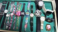 Photo showing an assortment of colorful and metal banded watches including digital and analog styles, pocket watch with chain, necklace watches, and themed watches.