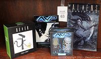 Four ALIEN-themed collectibles displayed: Lootcrate exclusive vinyl figure, AVP vinyl figures, Aliens Earth War comic book, and AVP creature effects sample book.