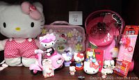 Wide shot of the Hello Kitty collection showing all items arranged together including plush, scooter, case, backpack, figurines, and PEZ dispenser.