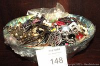 Overall view of a large basket containing assorted broken jewelry, showing various metal and beaded items inside a translucent plastic liner.