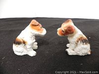 Side view of the two porcelain terrier dog figurines on a dark cloth background, showing their seated posture and detailing on fur and ears.