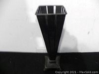 Full side view of the tall black metal decorative piece showing flared square top and narrow base with ornamental foot.