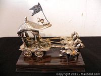 Side-angle image of brass chariot sculpture showing horses and rider.