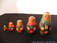 Set of five wooden nesting dolls arranged in size order on black background, showing hand-painted floral designs and faces.