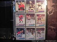 Photo of 9 hockey trading cards from 1976-77 O-Pee-Chee series showing players from Flyers, Bruins, Canadiens, and Capitals in a protective plastic sleeve in a 3 ring binder.