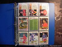 Photo of a blue binder with nine 1980-81 O-Pee-Chee hockey cards arranged in three rows, showing players from the Rangers, Sabres, Jets and others, clear and in protective sleeves.