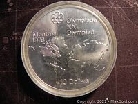 Obverse side of the coin showing the Montreal 1976 Olympics design with world map and Olympic rings.