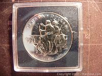 Reverse side of the 1990 Canadian silver 1 dollar coin depicting the voyageur and Indigenous canoe scene with inscriptions showing denomination and year.