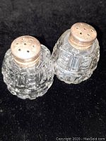 Pair of crystal salt and pepper shakers with sterling silver tops photographed on black background