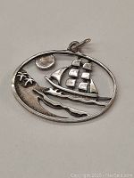 Front view of the oval sterling silver pirate ship pendant showing the ship with sails, sun, and wave design.