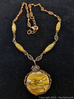 Front view of the sandstone pendant centered on the copper and sandstone bead chain, displayed on black background.