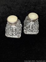 Pair of antique salt and pepper shakers with sterling silver tops and cut crystal bodies on black background.