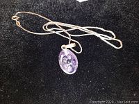 Single photo showing the sterling silver chain with an oval carved amethyst floral pendant on a black background.