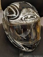 Front and side view of black, white, and gray full-face helmet with clear visor, showing HJC logo and graphic design.