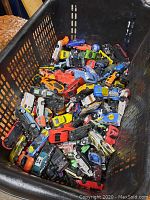 Plastic basket filled with a large assortment of toy cars in various colors and types.