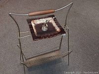 Shows the vintage metal wire magazine rack with wooden handle and ceramic ashtray feature on top.