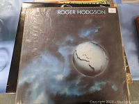 Two vinyl record covers stacked, top one 'In the Eye of the Storm' by Roger Hodgson with a globe storm image. Covers show signs of wear.