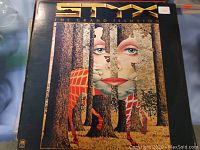 Photo of vinyl album cover of Styx's The Grand Illusion showing detailed artwork of a woman's face in forest design and band name
