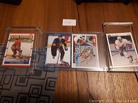 Three hockey cards laid out on a floor, each in a protective plastic case. Left card shows Eric Lindros 'Future Superstar' card, middle card is Alexander Daigle signed card, right card is another signed hockey card.