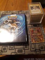 Black Pokemon TCG binder, loose stack of cards, Ancient Mew card on tabletop