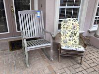 Front view of two outdoor chairs, one Adirondack with cushioned seat and one wooden rocking chair, on a tiled porch.